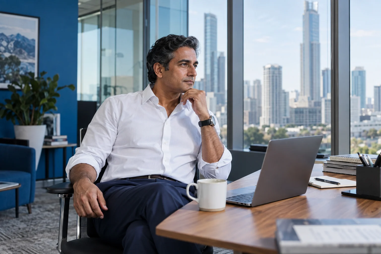 A man in a white shirt reflects at a desk overlooking the city.