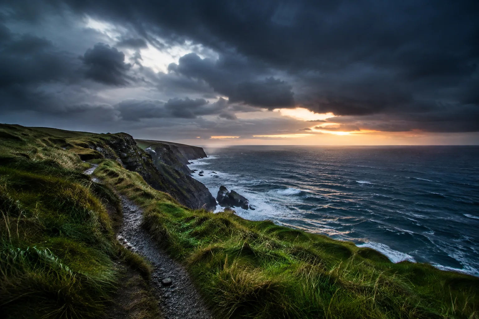 A coastal path leads toward a break of light over a stormy sea.