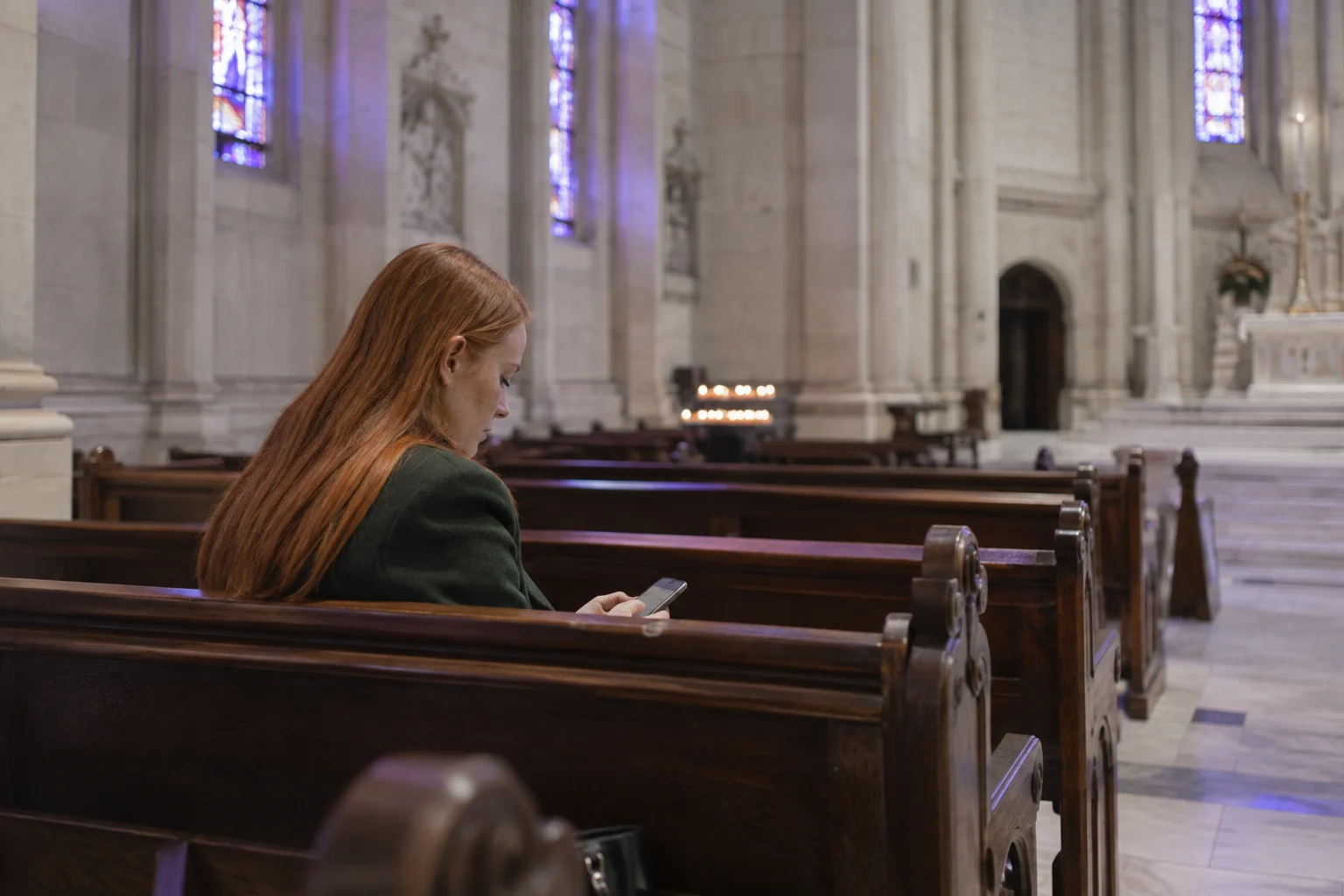 A red-haired woman sits with her phone in a quiet church sanctuary.